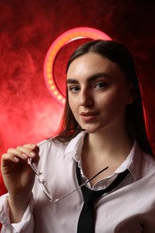 Photo of Beautiful woman with ring lamp and glasses on dark red background in smoke