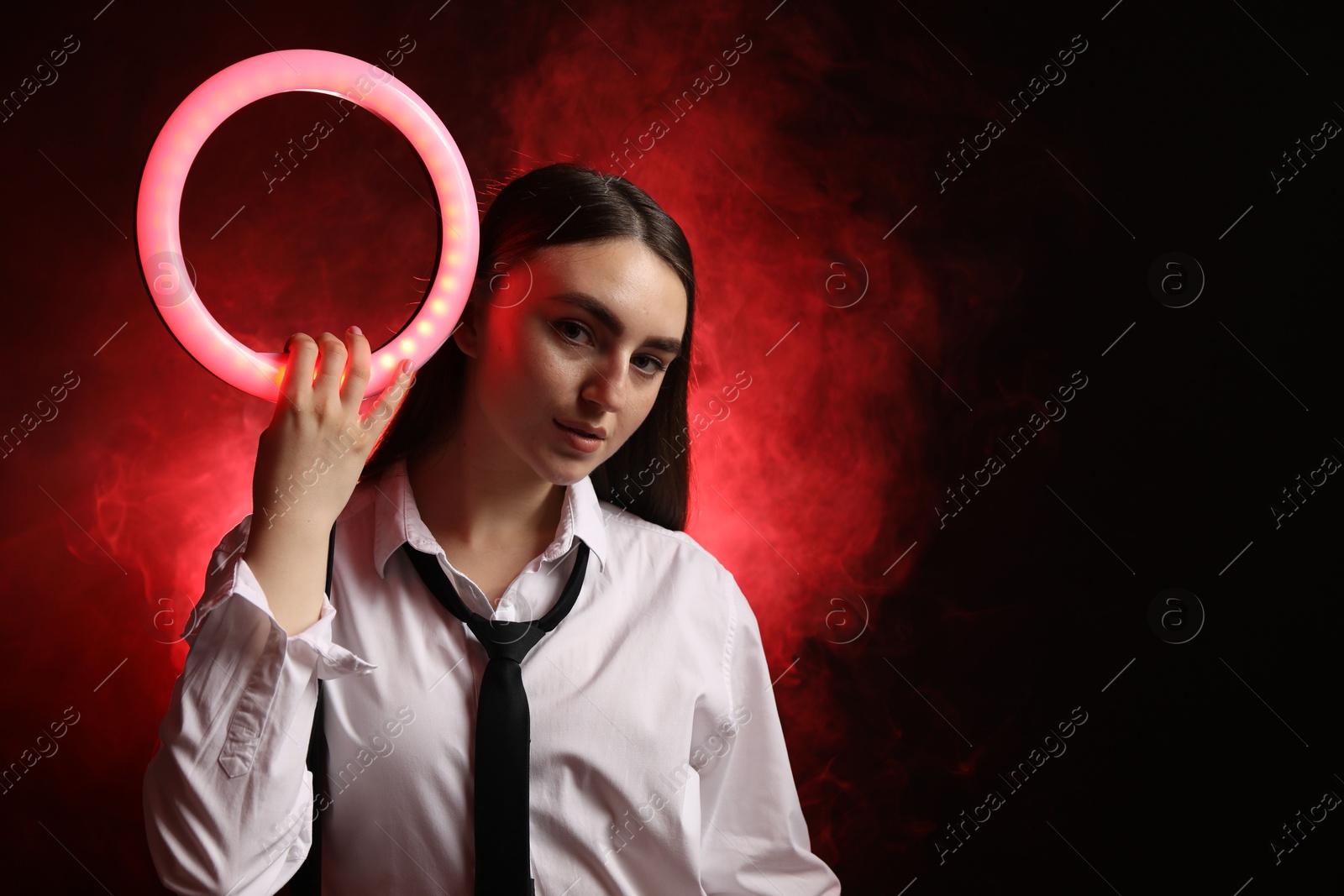 Photo of Beautiful woman with ring lamp on dark red background in smoke, space for text