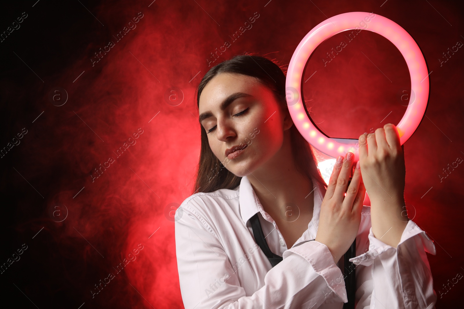 Photo of Beautiful woman with ring lamp on dark red background in smoke, space for text