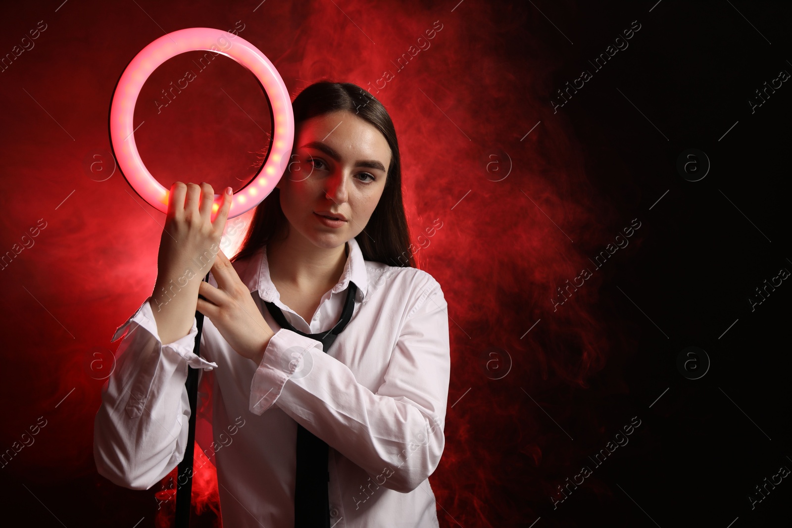 Photo of Beautiful woman with ring lamp on dark red background in smoke, space for text