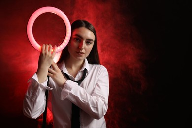 Photo of Beautiful woman with ring lamp on dark red background in smoke, space for text