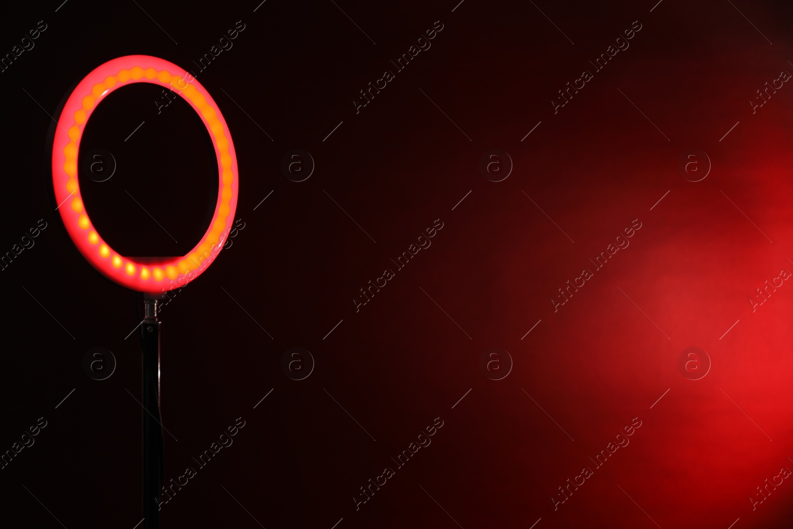 Photo of Ring lamp on stand against dark red background, space for text