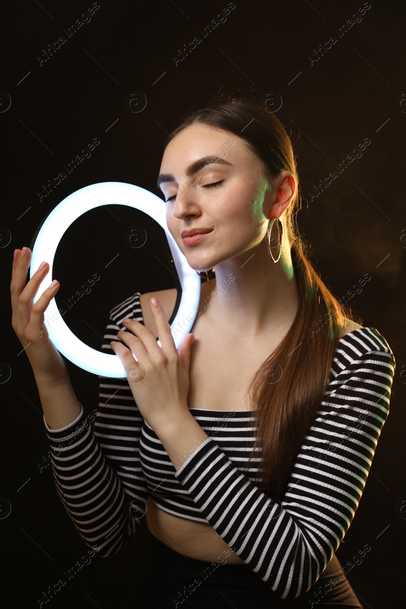 Photo of Beautiful woman with ring lamp on dark background in smoke