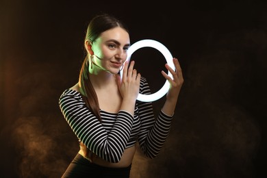 Photo of Beautiful woman with ring lamp on dark background in smoke, space for text