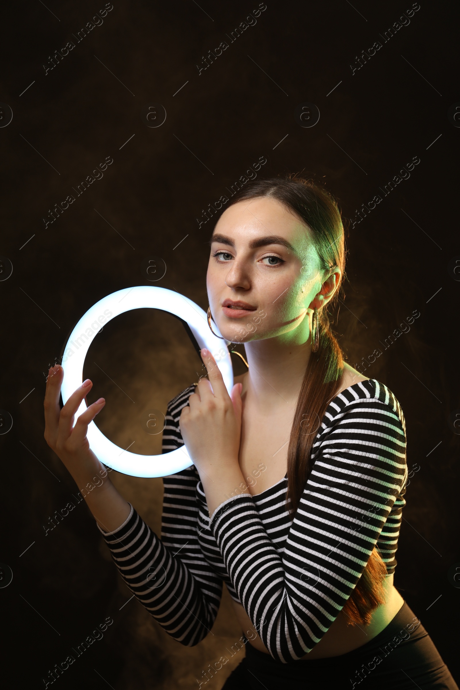 Photo of Beautiful woman with ring lamp on dark background in smoke