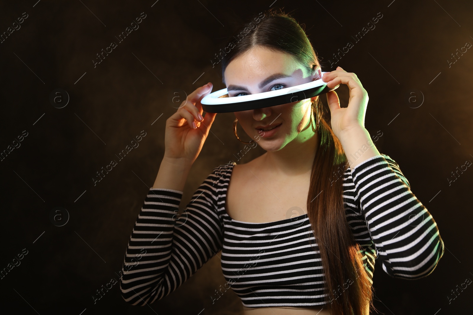 Photo of Beautiful woman with ring lamp on dark background in smoke, space for text