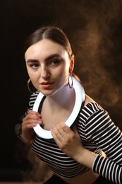 Photo of Beautiful woman with ring lamp on dark background in smoke