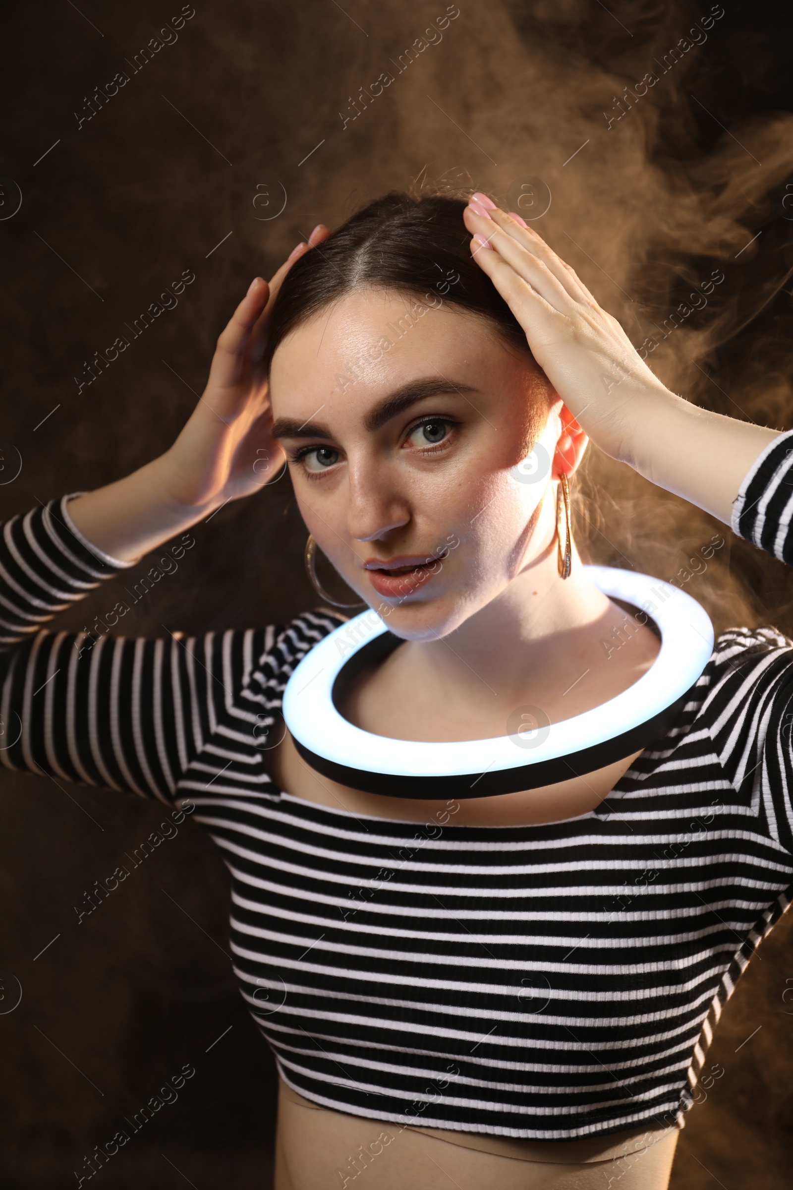 Photo of Beautiful woman with ring lamp on dark background in smoke