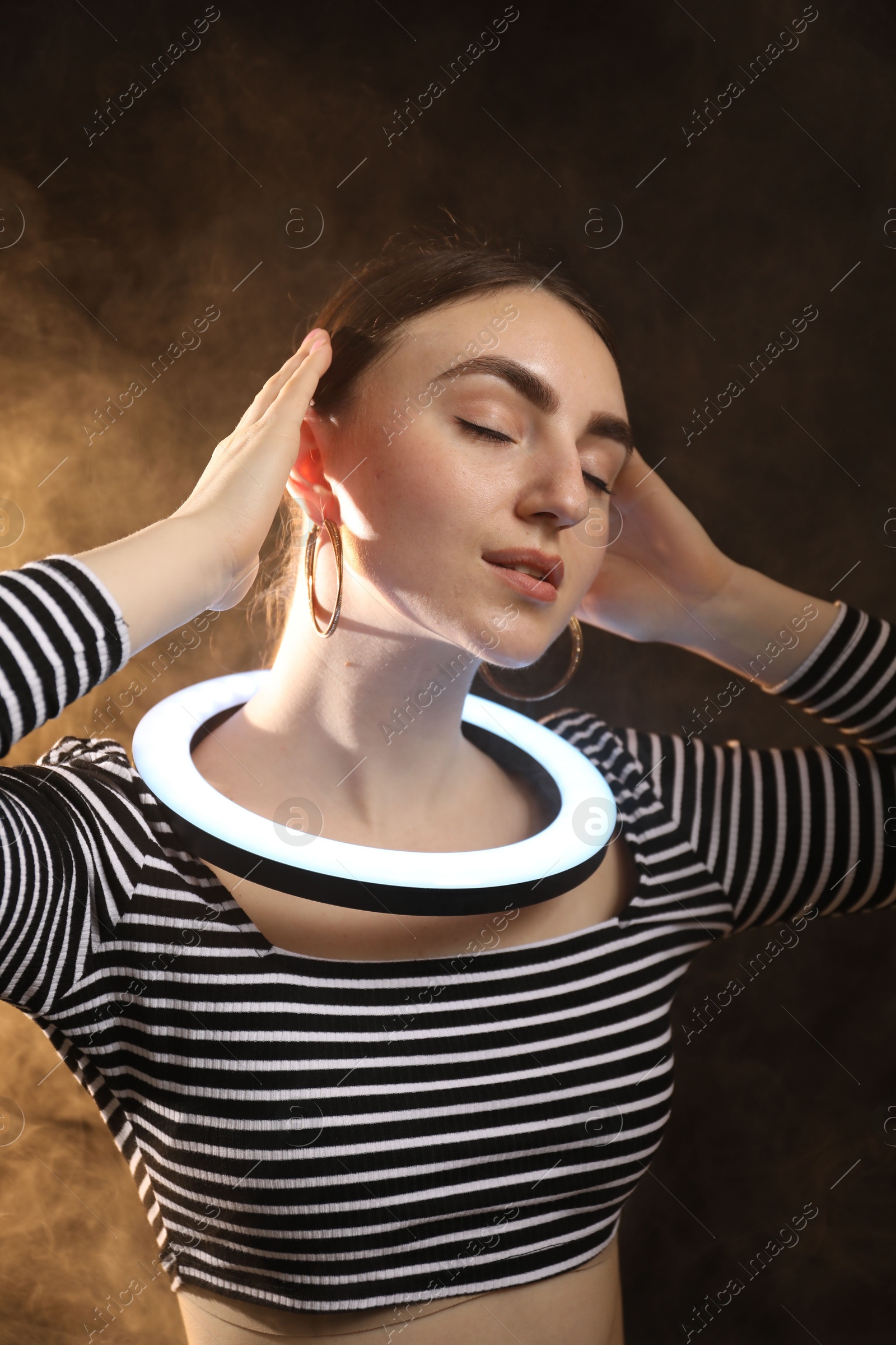 Photo of Beautiful woman with ring lamp on dark background in smoke