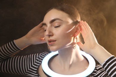 Photo of Beautiful woman with ring lamp on dark background in smoke