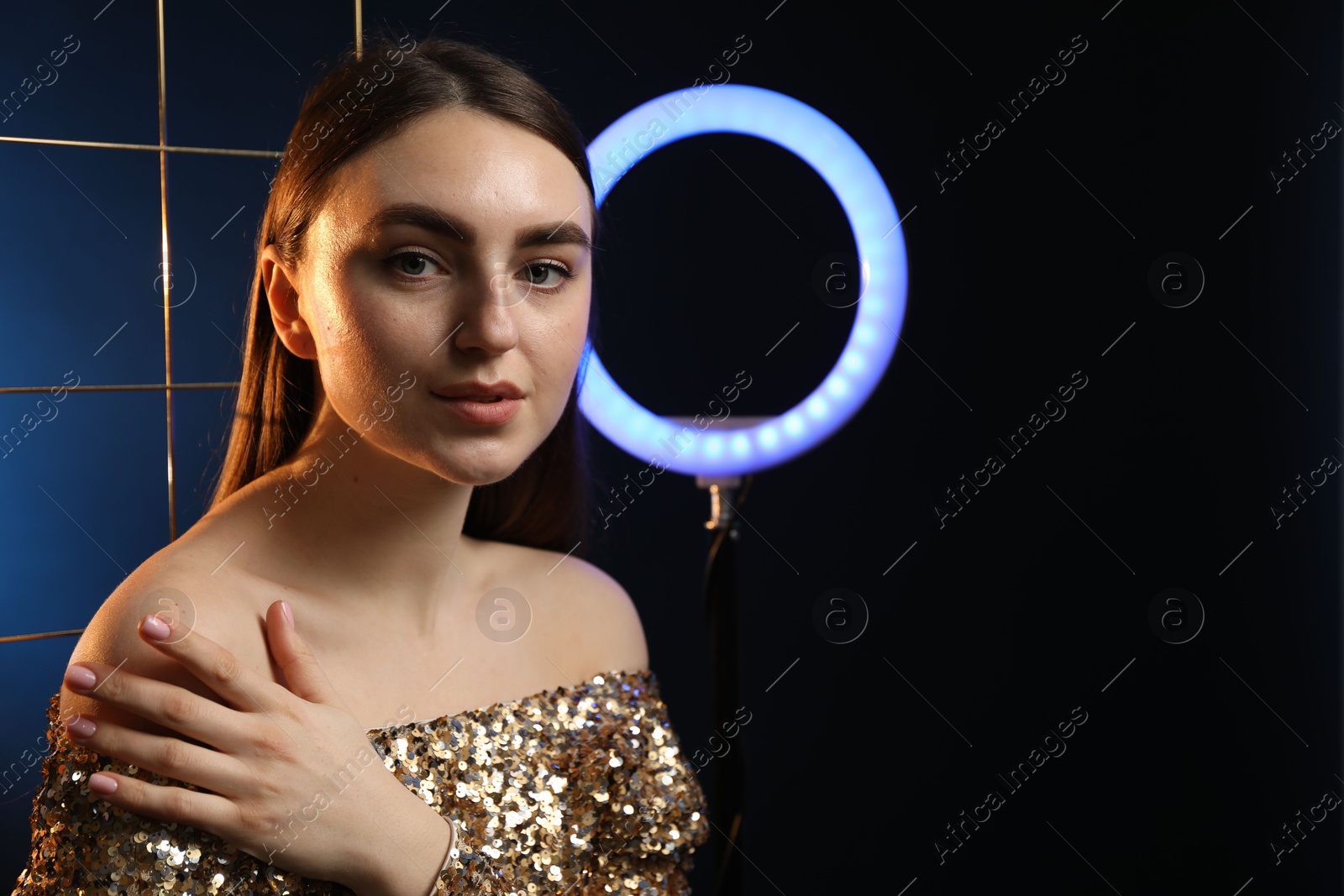 Photo of Beautiful woman with grid and ring lamp on dark blue background, space for text