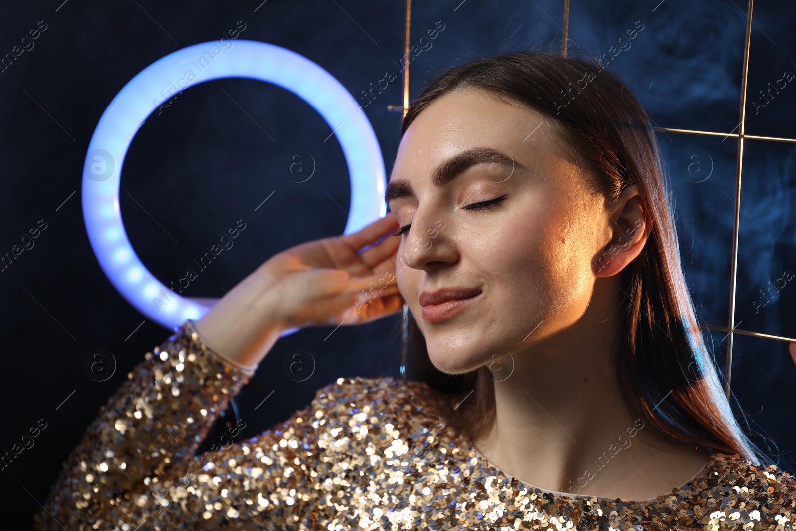 Photo of Beautiful woman with grid and ring lamp on dark blue background in smoke