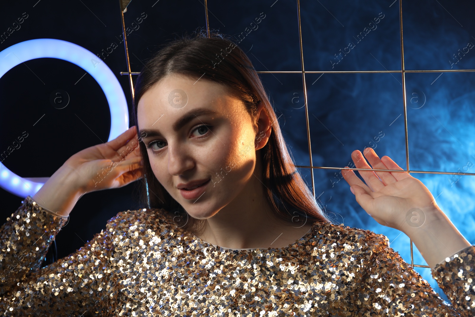 Photo of Beautiful woman with grid and ring lamp on dark blue background in smoke