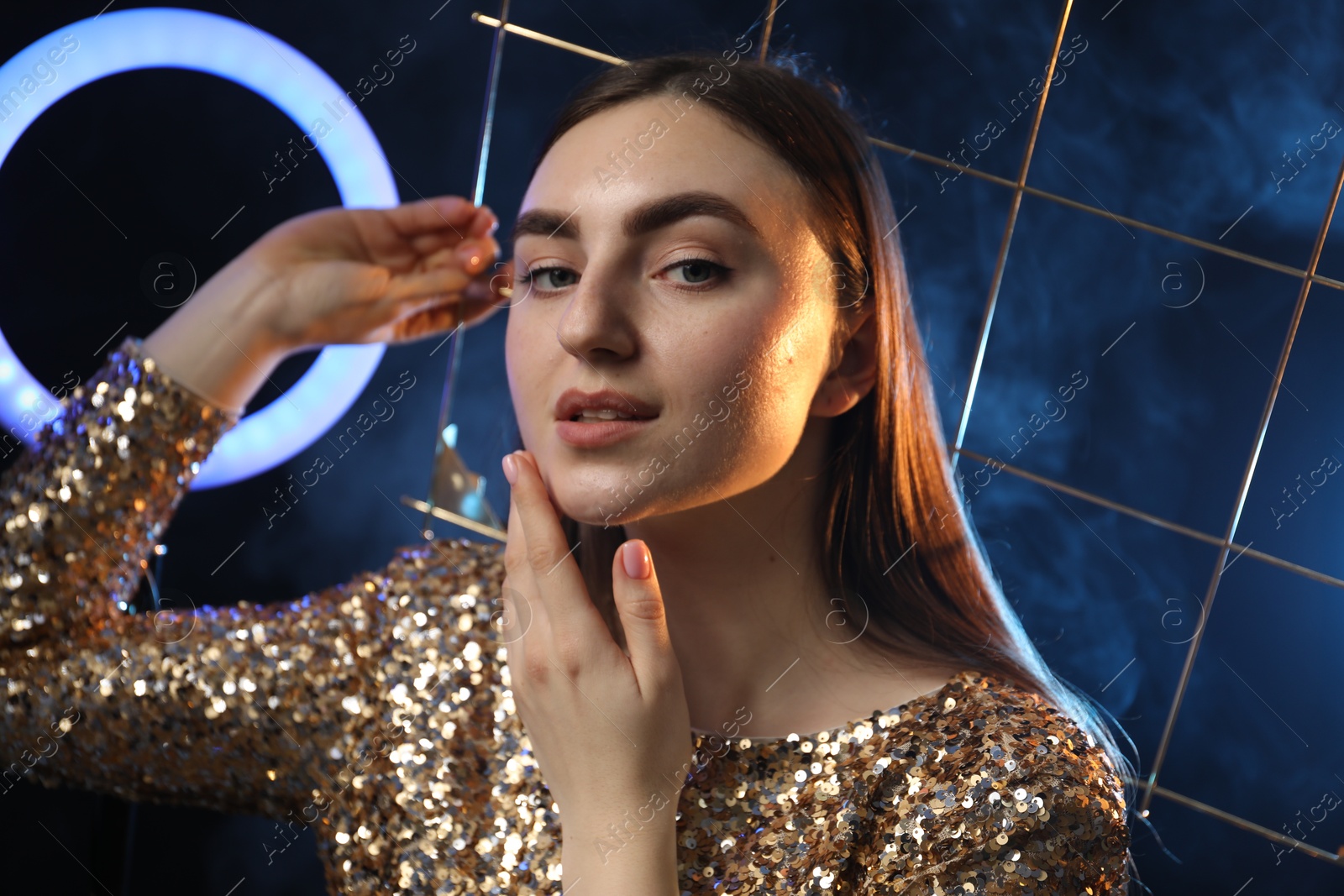 Photo of Beautiful woman with grid and ring lamp on dark blue background in smoke