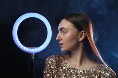 Beautiful woman with ring lamp on dark blue background in smoke