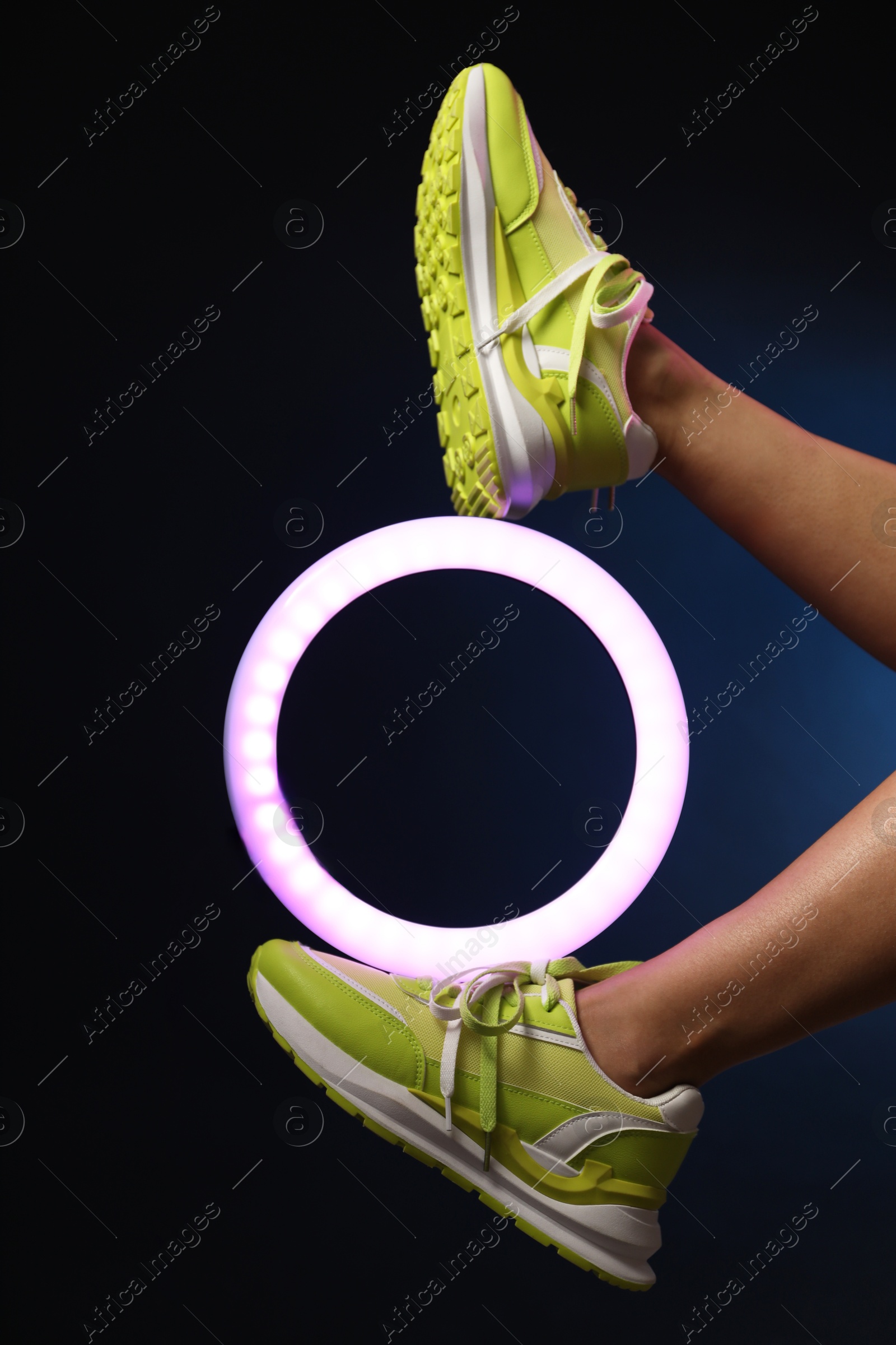 Photo of Woman with ring lamp wearing sneakers on dark blue background, closeup