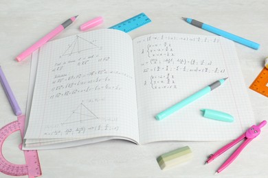 Photo of Doing homework. Notebook with math assignment and stationery on white desk, closeup