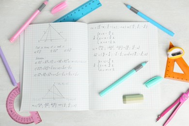 Photo of Doing homework. Notebook with math assignment and stationery on white desk, flat lay