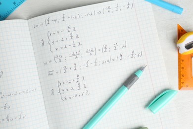 Photo of Doing homework. Notebook with math assignment and stationery on white desk, flat lay