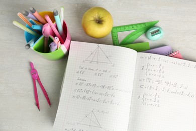 Photo of Doing homework. Notebook with math assignment, apple and stationery on white desk, flat lay