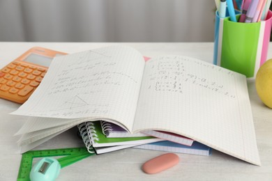 Photo of Doing homework. Notebook with assignment and stationery on white desk, closeup