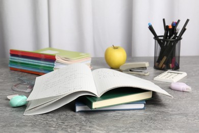 Photo of Doing homework. Notebook with math assignment, apple and stationery on grey desk