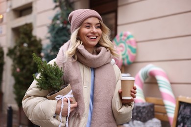 Photo of Happy woman with thuja tree and paper cup of coffee on city street. Christmas season