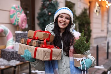 Photo of Happy woman with thuja tree and Christmas gifts on city street