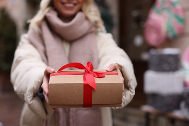 Photo of Woman with Christmas gift on city street, closeup. Space for text