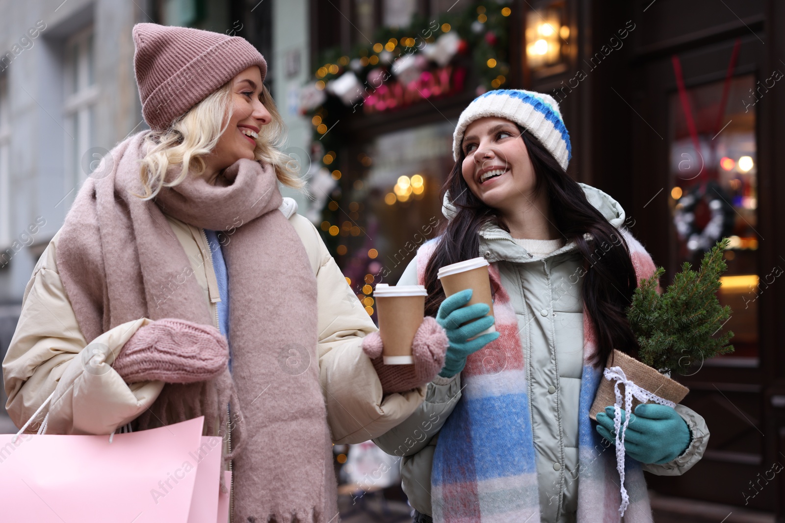 Photo of Happy friends with paper cups of coffee and thuja tree on city street. Christmas season