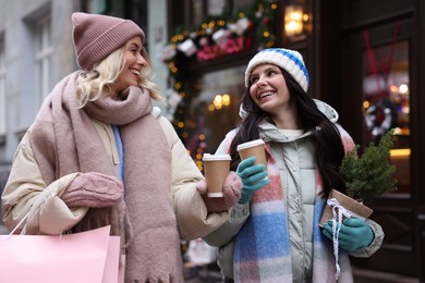 Photo of Happy friends with paper cups of coffee and thuja tree on city street. Christmas season