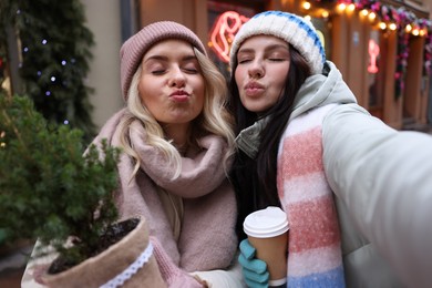 Photo of Happy friends with thuja tree and paper cup of coffee taking selfie on city street. Christmas season