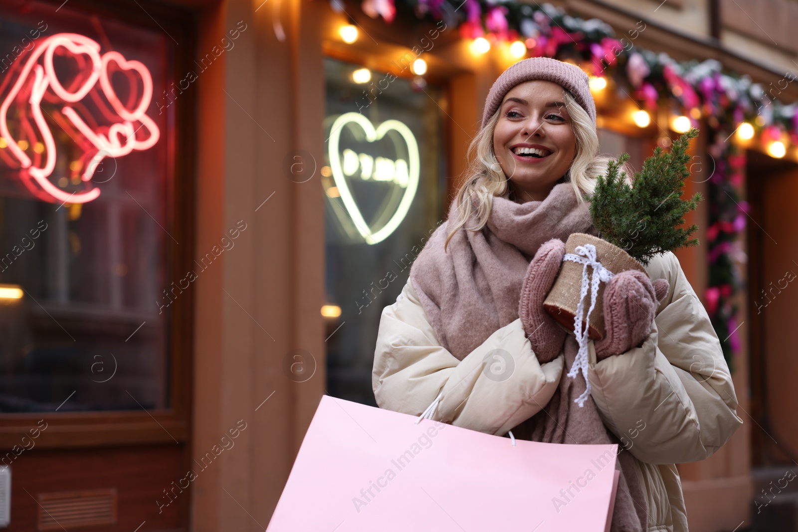 Photo of Happy woman with shopping bag and thuja tree near shop outdoors, space for text. Christmas season