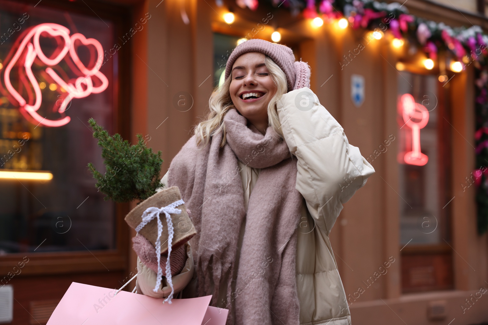 Photo of Happy woman with shopping bag and thuja tree near shop outdoors. Christmas season