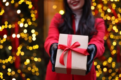 Photo of Woman with Christmas gift on city street, closeup. Space for text