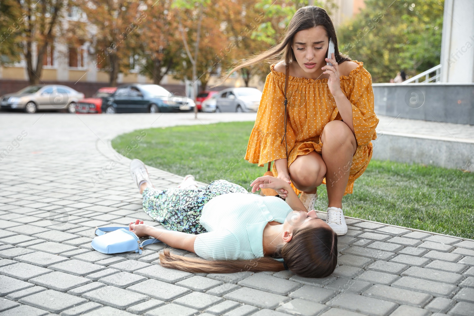 Photo of Woman calling ambulance to help unconscious person with heart attack on city street