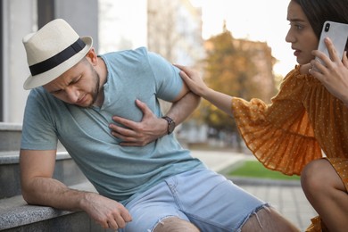 Photo of Woman calling ambulance to help man with heart attack on stairs