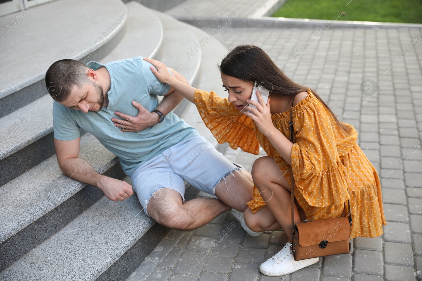 Photo of Woman calling ambulance to help man with heart attack on stairs