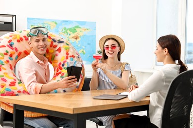 Photo of Happy couple planning vacation with travel agent at wooden table in office