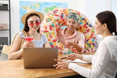 Photo of Happy couple planning vacation with travel agent at wooden table in office