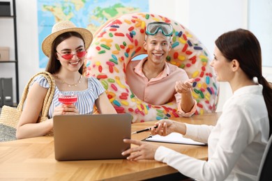 Photo of Happy couple planning vacation with travel agent at wooden table in office