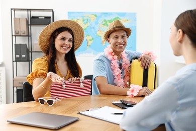 Happy couple planning vacation with travel agent at wooden table in office