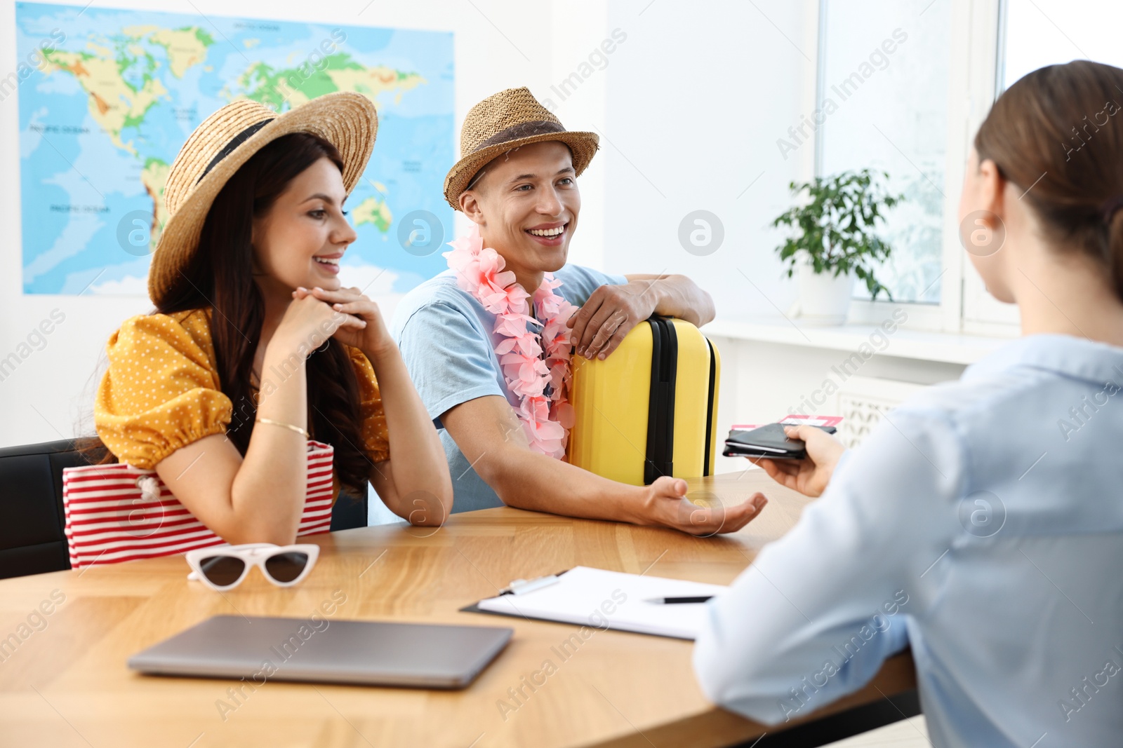 Photo of Happy couple planning vacation with travel agent at wooden table in office