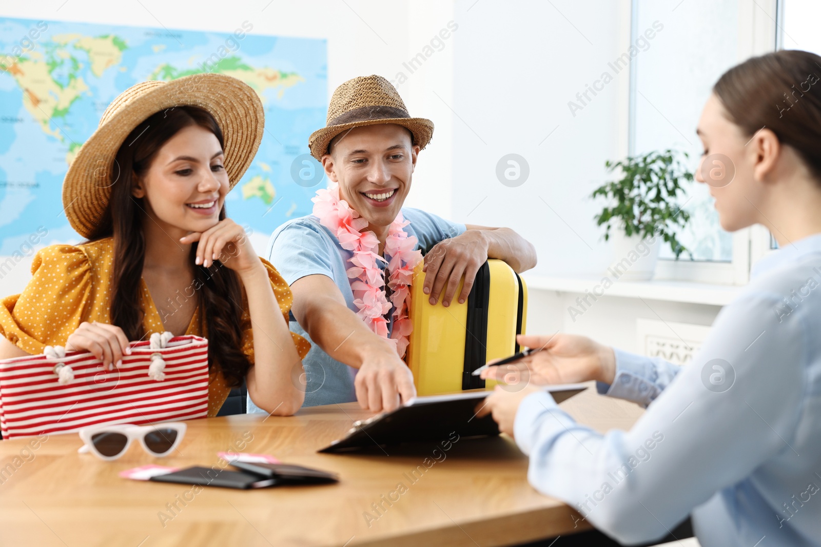 Photo of Happy couple planning vacation with travel agent at wooden table in office