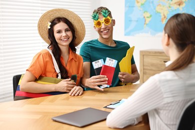 Photo of Happy couple planning vacation with travel agent at wooden table in office