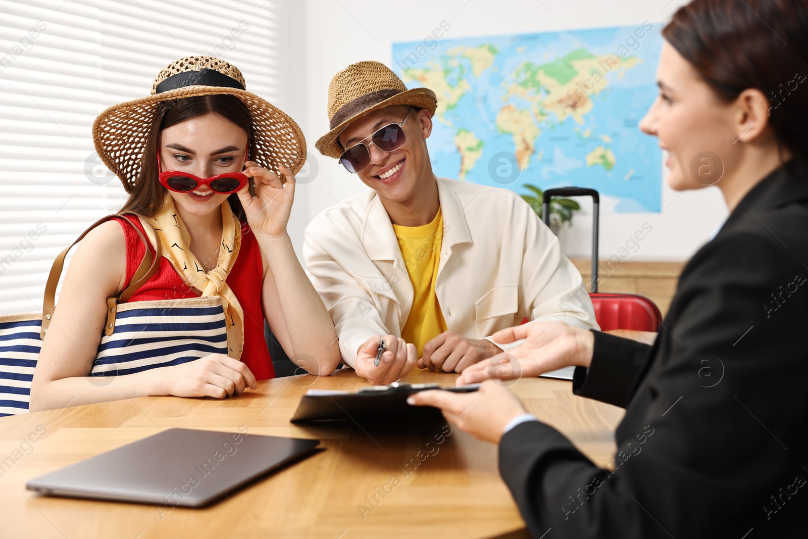 Photo of Happy couple planning vacation with travel agent at wooden table in office