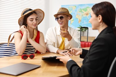 Photo of Happy couple planning vacation with travel agent at wooden table in office