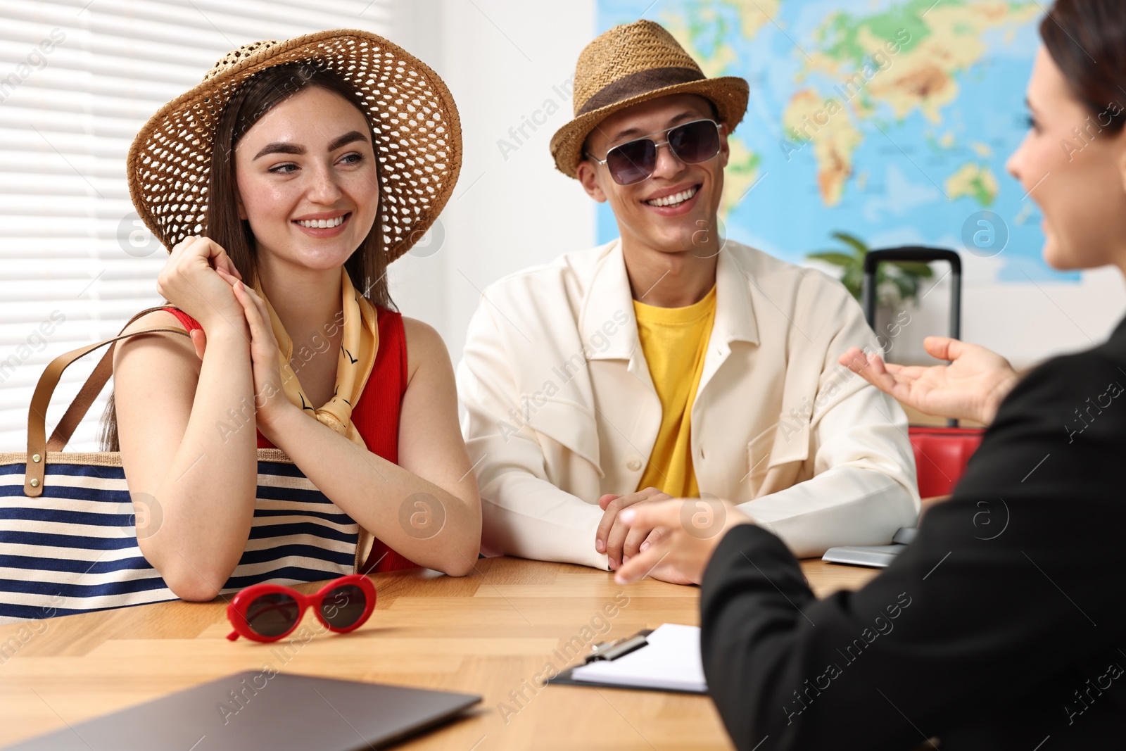 Photo of Happy couple planning vacation with travel agent at wooden table in office