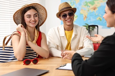 Photo of Happy couple planning vacation with travel agent at wooden table in office