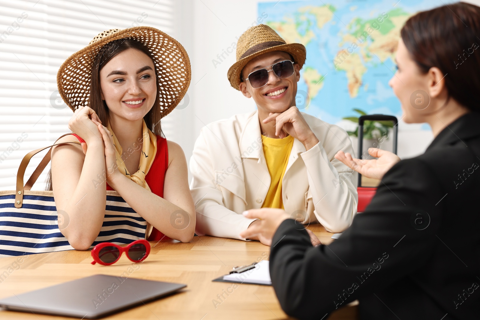 Photo of Happy couple planning vacation with travel agent at wooden table in office